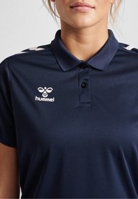 Námořnické modré polo tričko vyrobené z texturovaného materiálu, s tříknoflíkovou légou, vyšívaným logem a bílými akcenty na ramenou.