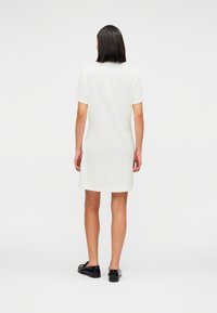 Λευκό βαμβακερό φόρεμα σε στυλ κοντομάνικου t-shirt, με ευθεία γραμμή και μήκος πάνω από το γόνατο. Μαύρα παπούτσια ολοκληρώνουν το σύνολο. Απλός, καθαρός σχεδιασμός.