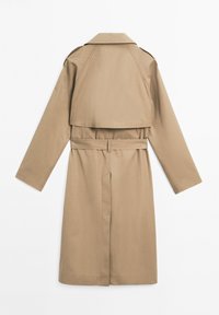 Beige Trenchcoat mit langen Ärmeln, tailliertem Gürtel und doppelreihigem Design. Der Stoff wirkt glatt und hat einen klassischen Kragen.