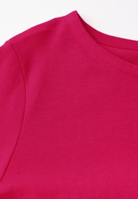 Fuchsiová košile s krátkým rukávem vyrobená z hladkého materiálu. Má kulatý výstřih a viditelné švy podél okrajů.