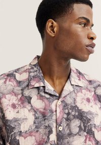 Kurzärmliges Hemd mit Knopfleiste aus Stoff, das mit einem mehrfarbigen Blumenmuster in Lila-, Rosa- und Grautönen versehen ist.