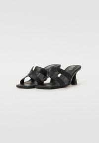 Svarte hæler med mules som har en jevn lærtekstur, åpen tå-design og to frontremmer med utskjæringer.