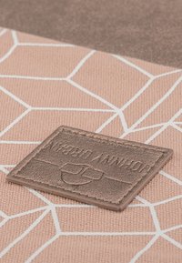 Textúrovaná látka v tlmenej ružovej farbe s geometrickými bielymi vzormi; obsahuje vyvýšenú hnedú koženú nášivku s embosovaným logom.