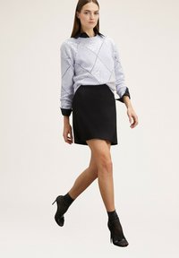 Maglione azzurro chiaro con motivo a rombi e paillettes, abbinato a una mini gonna nera. Calze alla caviglia nere trasparenti a pois e tacchi.