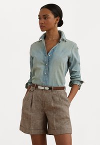 Šviesiai mėlynų džinsų marškiniai su smailiu apykakle, derinami su rudais languotais šortais su klostėmis ir derančia diržu.