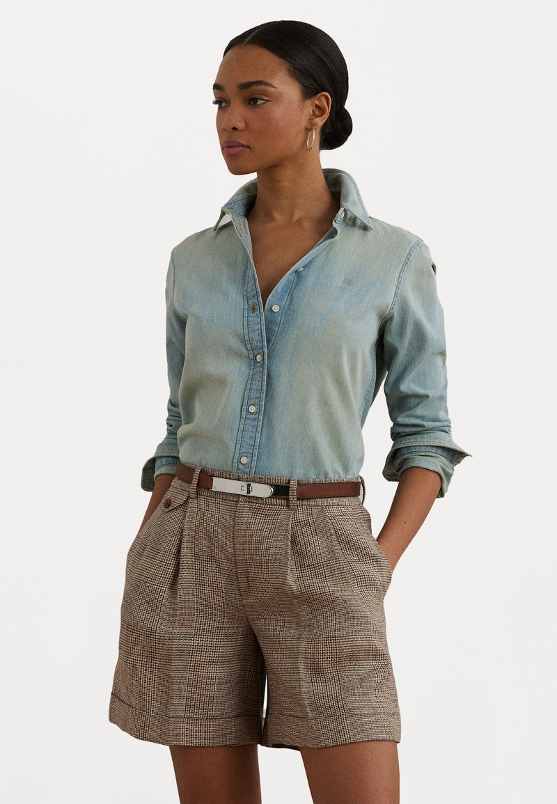 Šviesiai mėlynų džinsų marškiniai su smailiu apykakle, derinami su rudais languotais šortais su klostėmis ir derančia diržu.