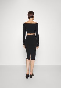 Černý krátký top s dlouhým rukávem a přiléhavou sukní se bočním rozparkem, vyrobený z elastického materiálu, s hladkou texturou a jednoduchým designem.