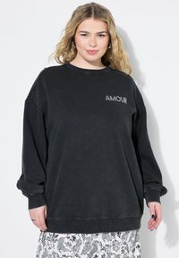 Svart sweatshirt med rund halsringning, sänkta axlar och textdetalj "AMOUR" i grått. Mjukt, texturerat tyg med avslappnad passform.