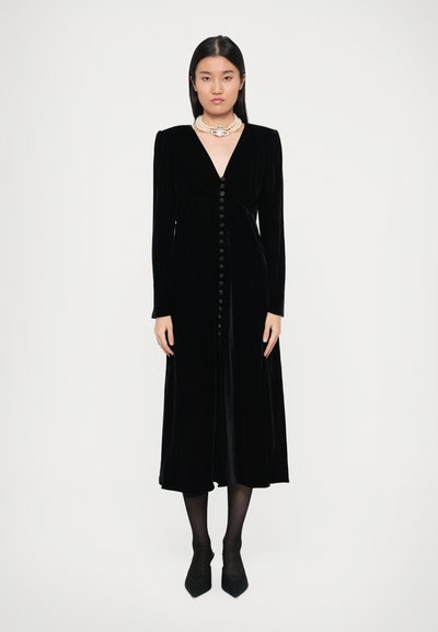 Robe longue en velours noir à manches longues avec décolleté en V, présentant une rangée de boutons sur le devant. Texture lisse et corsage ajusté avec un ourlet fluide.