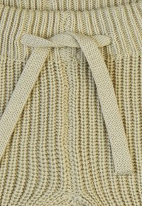 Beige gebreide stof met een opvallend ribbelpatroon, voorzien van een vlak geweven koord dat in een strik is geknoopt op de taille.