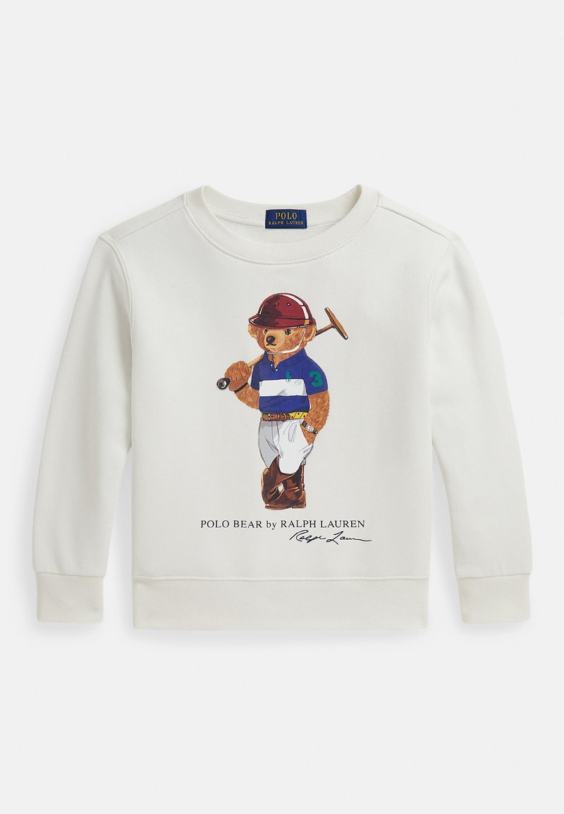 Krém színű pulóver, amelyen egy medvét ábrázoló grafika látható, amint polo ruhában egy polo ütőt tart, alatta a "Polo Bear by Ralph Lauren" felirattal.
