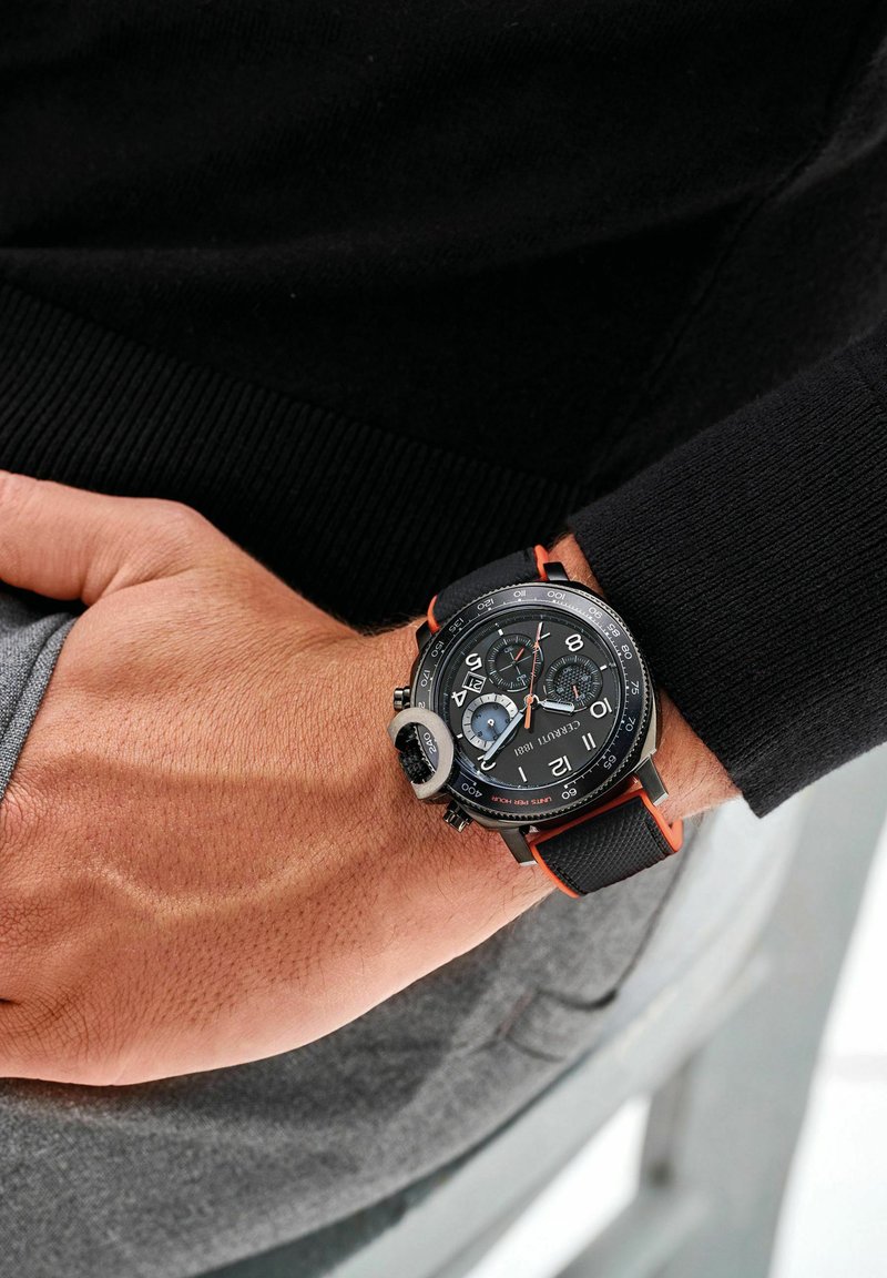 Orologio cronografo nero con accenti arancioni, cinturino testurizzato, grandi numeri, sottocompiti e una cassa resistente. Indossato su un polso contro un indumento scuro.