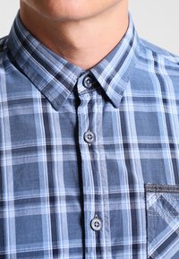 Camicia a maniche corte a quadri blu e blu navy con colletto button-down, caratterizzata da un motivo a scacchi e una tasca a toppa sul lato sinistro.
