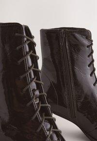 Sorte ankelstøvler i laklæder med snørelukning foran og lynlås på siden. Glat tekstur med elegant design og en let spids tå.