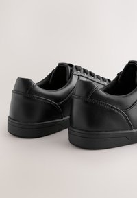 Sneakers in pelle nera con una texture liscia, punta arrotondata, lacci minimi e suola in gomma dal profilo basso. Sottili dettagli di cucitura sui lati.