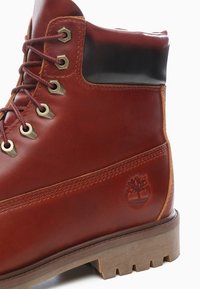 Brun läderankelboot med rundad tå, metallöglor och gummisula. Svarta läderdetaljer vid kragen. Timberland-logotyp präglad.