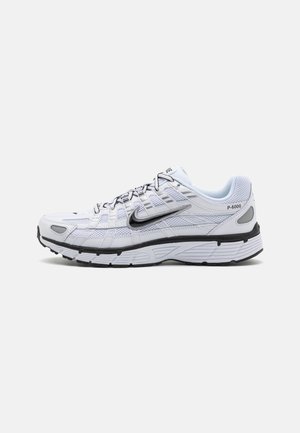 Witte Nike P-6000 hardloopschoen met zwart swoosh-logo, zwart-witte zool en bovenwerk van mesh en leer, zijaanzicht op een witte achtergrond.