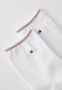 Calcetines blancos hasta la rodilla con acentos de rayas rojas y negras en la parte superior y un pequeño detalle de logo en el costado. Fabricados con un material de punto texturizado.