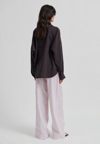 Chemise oversize marron foncé à manches longues associée à un pantalon large à jambes larges rose clair à rayures verticales. Tissu lisse et coupe décontractée.