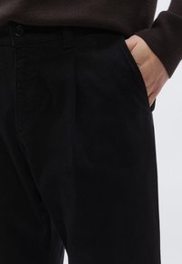 Juodos spalvos korduro kelnės su struktūruotu paviršiumi, tiesaus silueto su šoninėmis kišenėmis. Liemuo turi sagą užsegimui.