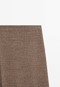 Gros plan d'une section de tissu tricoté marron avec de fines coutures et une texture chinée sur un fond blanc uni.