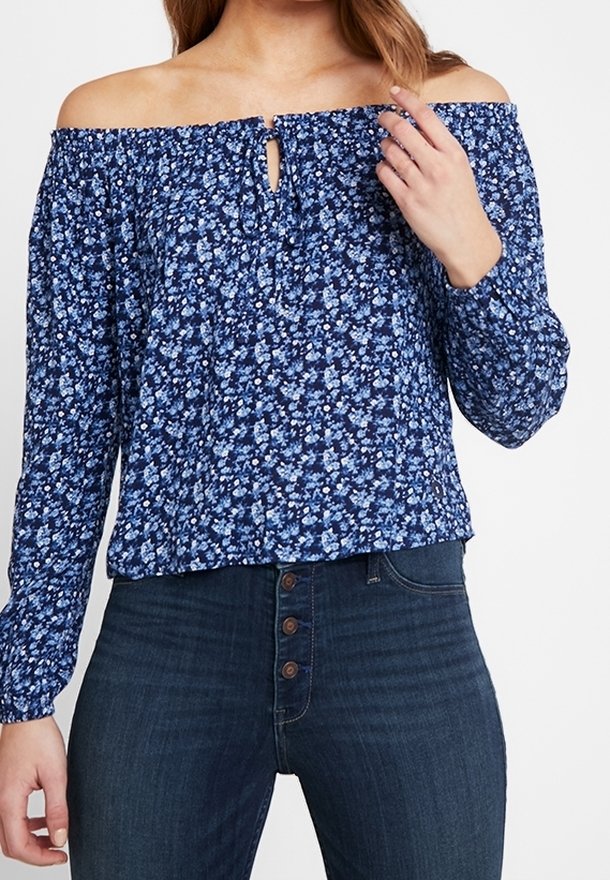 Blue floral off-the-shoulder blouse with a gathered neckline, featuring small buttons at the front and long sleeves, paired with dark jeans.