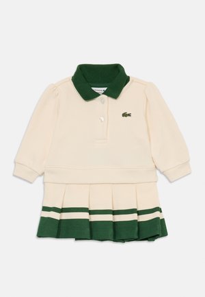 Cremefarvet polo kjole med lange ærmer og grøn krave, to knapper, plisseret nederdel med grønne og cremefarvede striber samt et lille logo på brystet.