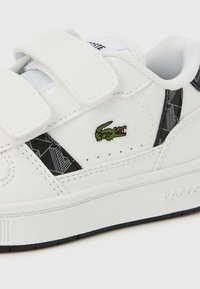 Λευκό δερμάτινο αθλητικό παπούτσι με λουριά βέλκρο, που διαθέτει πράσινο κεντημένο λογότυπο κροκόδειλου και μαύρο γεωμετρικό σχέδιο στο πλάι.