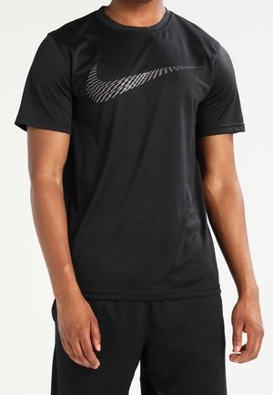 Person trägt ein schwarzes Nike-T-Shirt mit einem großen, gemusterten weißen Swoosh-Logo auf der Brust, kombiniert mit schwarzen Shorts.