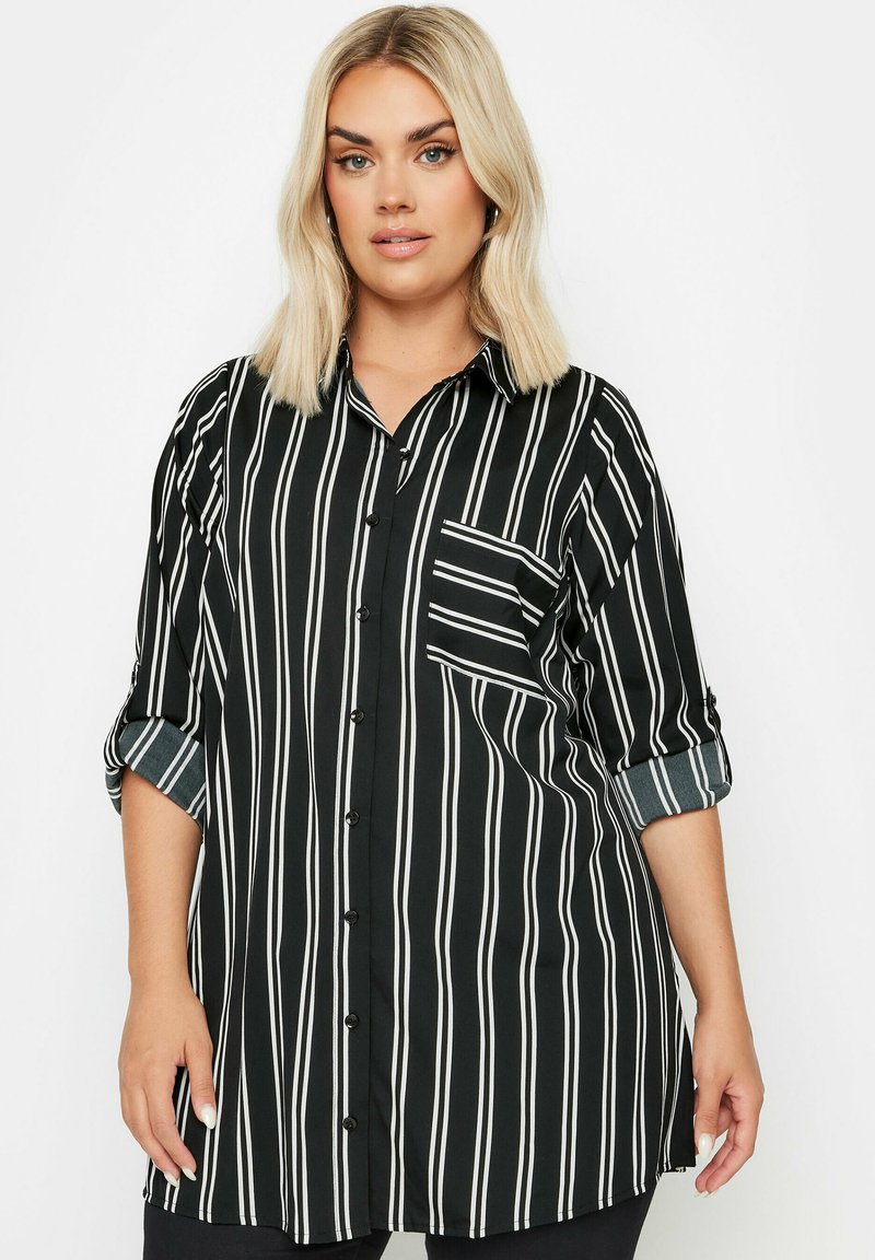Camicia a righe bianche e nere con chiusura a bottoni, maniche lunghe, tasca sul petto e polsini arrotolati. Tessuto morbido.