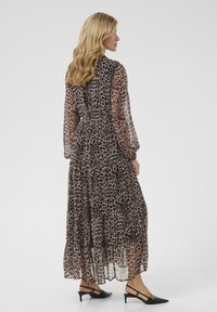 Robe maxi en tissu léger et transparent avec un motif léopard. Présente des manches longues et une jupe à volants, associée à des talons noirs.