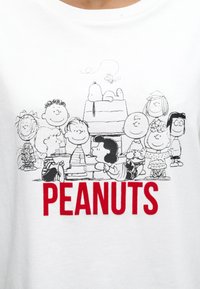 Εννέα χαρακτήρες κινουμένων σχεδίων Peanuts συγκεντρώνονται γύρω από τον Snoopy στο σκυλόσπιτό του, με τη λέξη "PEANUTS" με έντονα κόκκινα γράμματα από κάτω.