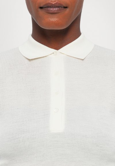 Polo shirt a maniche corte, di colore crema, realizzato in tessuto a costine con patta dei bottoni e colletto liscio a punta.