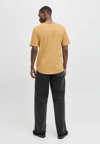 Sennepsgul t-shirt med korte ærmer og rund hals, parret med løse sorte denim jeans. Stoffet virker blødt med en glat tekstur.