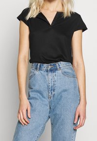 Svart kortärmad topp med V-hals och en mjuk textur, tillsammans med högmidjade ljusblå denimjeans med en lätt urtvättad finish.