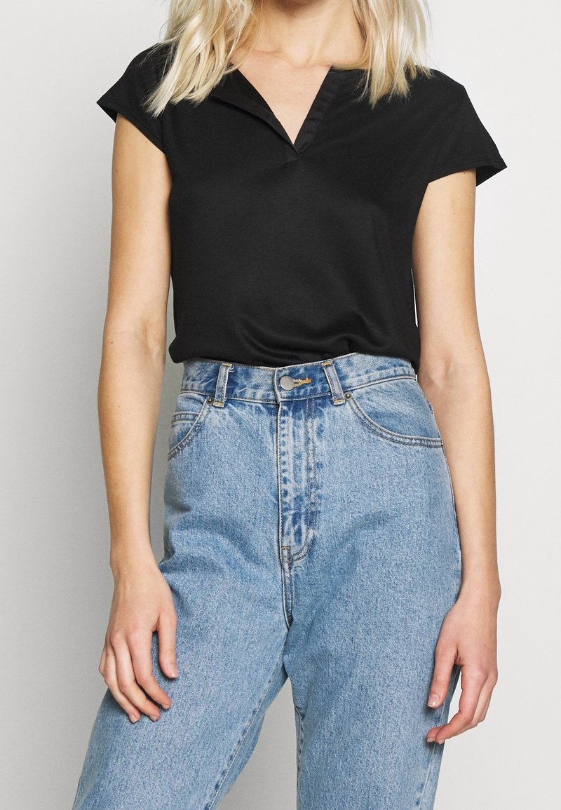 Svart kortärmad topp med V-hals och en mjuk textur, tillsammans med högmidjade ljusblå denimjeans med en lätt urtvättad finish.