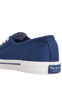 Mornarsko platneno športno obuvalo s belim gumijastim podplatom, okroglo konico, vezalkami in logotipom v kontrastni barvi na peti.