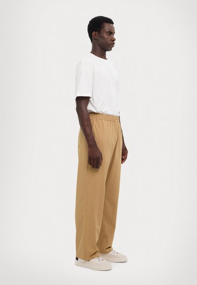 Un pantalon beige, à coupe décontractée, avec une taille élastique et des poches latérales, assorti à un t-shirt blanc uni et des baskets blanches.