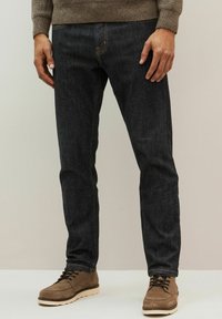 Jeans din denim închis, cu cusături portocalii, croială slim fit, cu picioare drepte, asortați cu cizme din suede maronii și un pulover texturat.