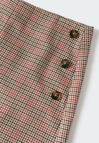 Tissu pied-de-poule marron, noir et rouge avec trois boutons en écailles de tortue foncées alignés verticalement près du bord.
