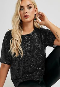 Svart paljetttopp med korta ärmar, med rund halsringning. Glittrande yta med täta, små paljetter. Avslappnad och ledig passform.