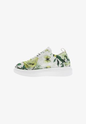 Zapatilla blanca con suela gruesa que presenta una superposición de encaje floral verde y amarillo, con cordones blancos, mostrada en perfil lateral.