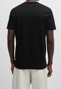 Černé tričko s krátkým rukávem a kulatým výstřihem, vyrobené z bavlny. Hladká textura, jednoduchý design bez viditelných vzorů nebo log, zobrazený zadní pohled.