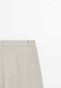 Pantalon en lin beige clair avec passants pour ceinture, taille visible et tissu texturé sur fond blanc.