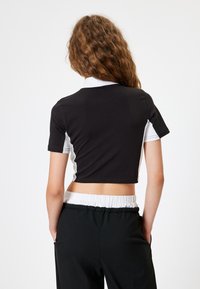 Geknipte zwarte shirt met witte kraag en zijkanten, korte mouwen, gladde textuur. Gecombineerd met zwarte broeken met elastische tailleband.