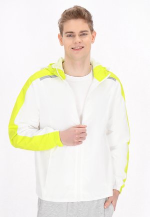 Valkoinen takki, jossa on kirkas limevihreä korostus hupussa ja hihoissa. Ominaisuuksiin kuuluu vetoketjusuljenta ja joustavat hihansuut. Mallilla on alla valkoinen paita.