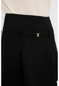 Schwarzer Rock mit einem eleganten Design und einem dünnen, goldfarbenen Akzentgürtel. Hergestellt aus glattem Stoff, hat er einen strukturierten Bund und maßgeschneiderte Falten.