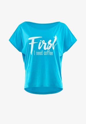 Tirkizna majica kratkih rukava s opuštenim krojem. Sadrži bijeli natpis "Prvo trebam kavu." Mekani, lagani materijal s okruglim izrezom.