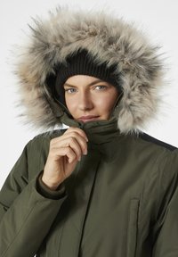 Parka verde oliva con capucha de borde de piel sintética, cierre de cremallera y puños de punto acanalado. Cuenta con un bolsillo lateral y una tela de acabado suave y mate.