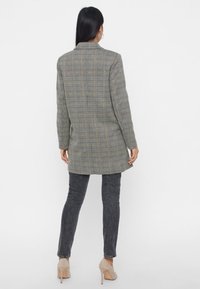 Šedý kostkovaný blejzr s přiléhavým střihem, dlouhou siluetou, klopami s výstřihem a jedním zadním rozparkem, spárovaný s tmavými džíny.